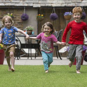 Three happy kids running on artificial grass.